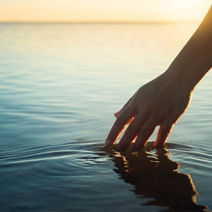 Photograph of a hand dipping into the ocean at sunrise.