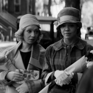 A black and white photo of two women wearing 1920s era outfits and carrying flowers