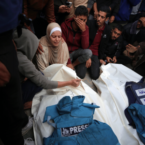 The photo shows mourning Gazans as they stand over the covered bodies of two slain journalists, their blue press vests resting on their bodies. 