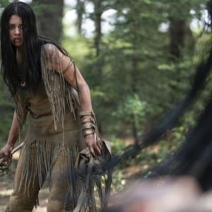 A Comanche woman stands in a combat-ready pose with a tomahawk against an assailant in the film 'Prey.'