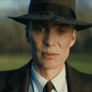 A photo shows a white man wearing a suit and a bowler hat looking into the camera seriously 