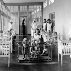 Black and white image of nuns in a "mother and baby home" line a room filled with children in several cribs