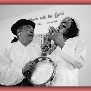 A vintage photo of two Black women laughing and playing instruments in church.