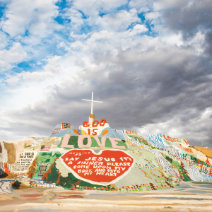 The image shows a large colorful hill with a cross on top that has a heart and says "God is Love" 