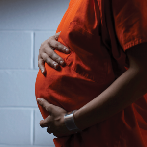 The image shows the pregnant belly of a woman in prison, wearing an orange uniform. She is black. 