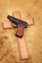Gun laying on top of a wooden cross. Photo courtesy RNS/iStockPhoto. Photo courtesy RNS/iStockPhoto.