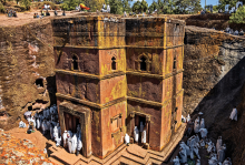 the photo is a image of a red church carved out of rock. The church has pilgrims surrounding it, all of them wearing white