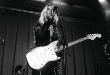 Black and white photo of Natalie Bergman holding an electric guitar and singing into a mic stand