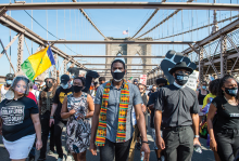 Jumaane Williams walks in front of a group of masked Black people crossing the Brooklyn Bridge