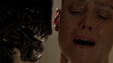 A close-up screenshot from Alien 3; an alien creature with its mouth open is seen from the side, with its teeth next to the shiny face and ear of a white woman who directly faces the camera.