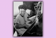 A portrait of Mary Lou Williams playing the piano and smiling.