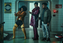 The picture shows three black youth, dressed in colorful outfits and pointing handguns at something off screen. 