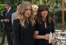 A picture from the TV show ‘Dead to Me’ of Jen (Christina Applegate) and Judy (Linda Cardellini) in black dresses as they stand side by side with arms locked.