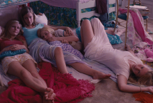 The image shows four girls lounging on the floor, they are sisters. The room is full of pink items. 