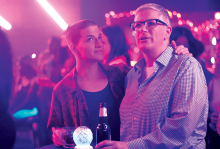 A scene from 'Work In Progress' shows Abby, the main character, at a club in pink light.