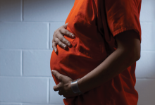 The image shows the pregnant belly of a woman in prison, wearing an orange uniform. She is black. 