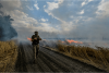 A Ukrainian serviceman holds a gun while walking through a burning wheat field.