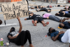 Protesters lie on pavement. One holds a sign that says "We Are Tired of This."