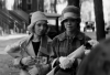 A black and white photo of two women wearing 1920s era outfits and carrying flowers