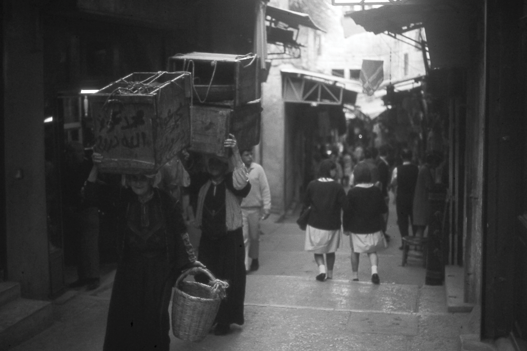 Women carrying boxes of produce on their heads and school girls walking through the Armenian Quarter in Old City Jerusalem, November 1967.